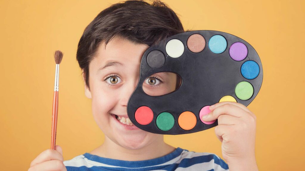 Lächelnder Junge mit einer Farbpalette und einem Pinsel