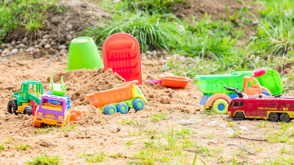 Buntes Kinderspielzeug wie z.B. Lastwagen und Traktoren im Sand