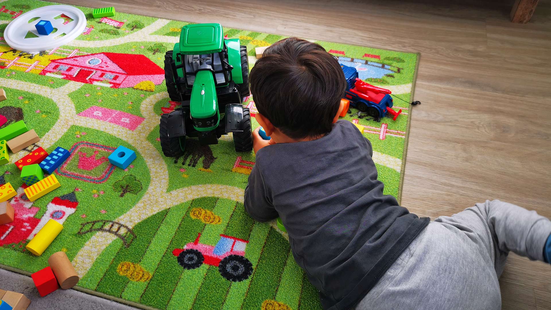 Unser kleiner Sohn spielt mit einem seiner geliebten großen grünen Spielzeugtraktoren