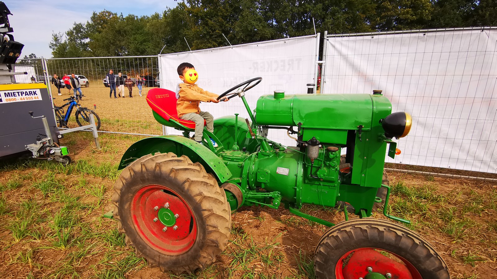 A child sitting on an old green vintage tractor at a tractor show