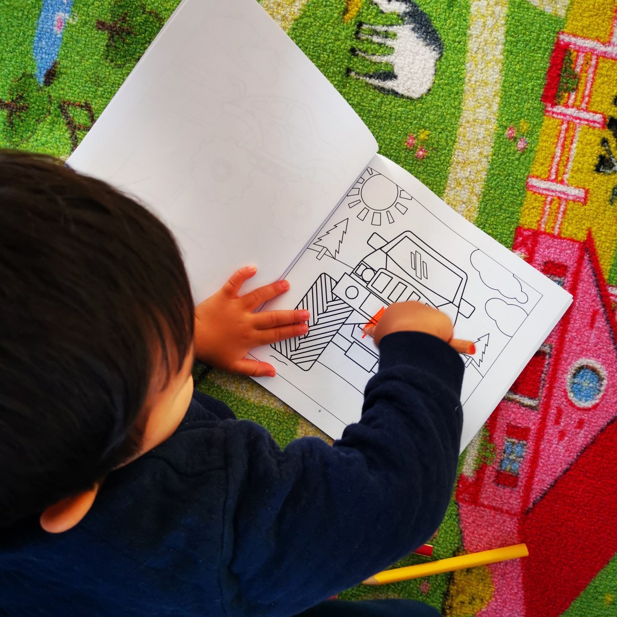 Young child coloring a monster truck page from a coloring book