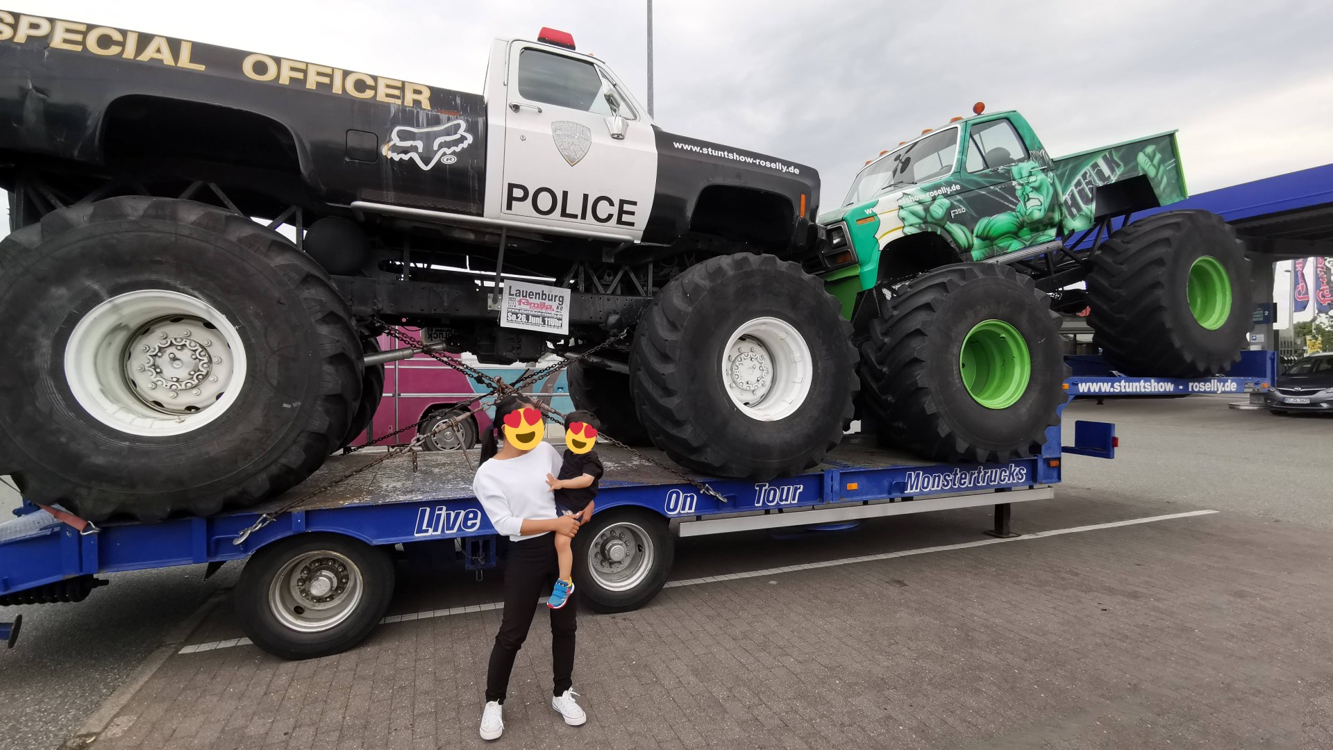 Young child standing beside giant monster trucks at a live vehicle show