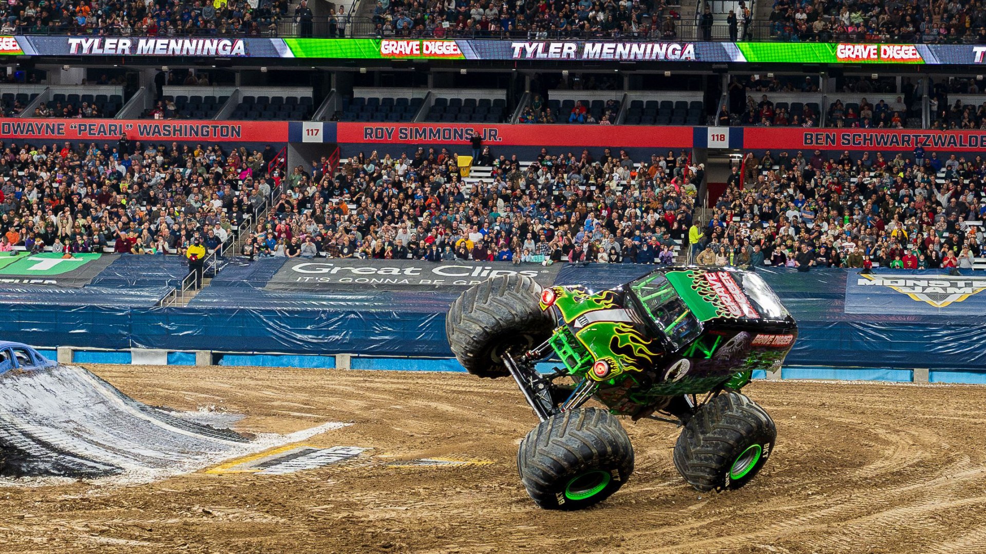 Green monster truck performing a two-wheel stunt in a packed arena