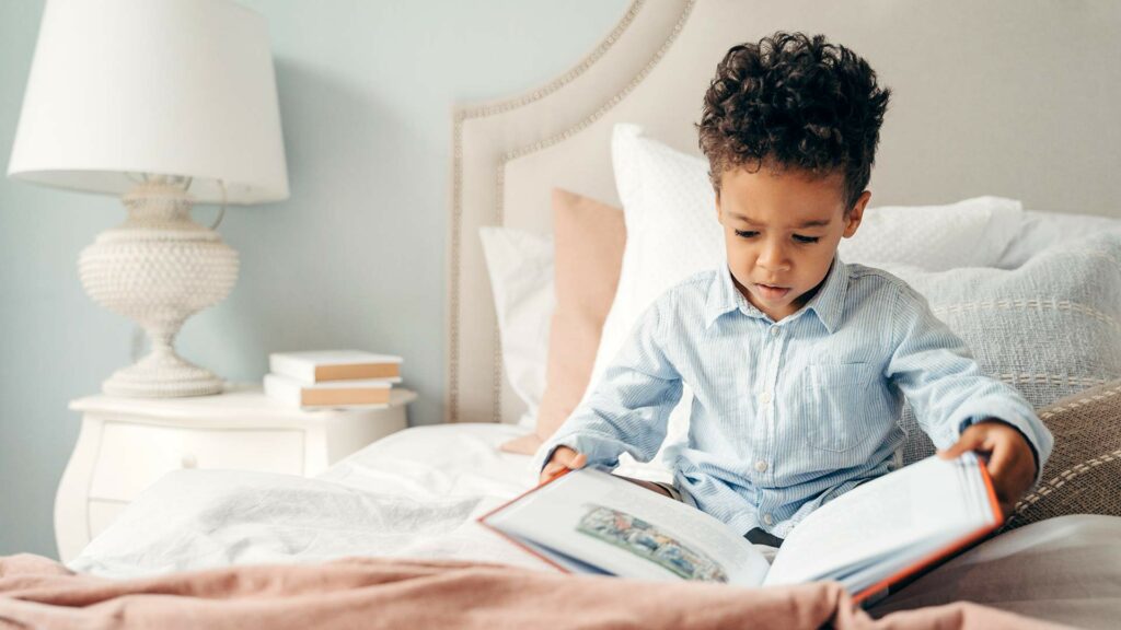 Cute Afro-American boy reading a book in his bed